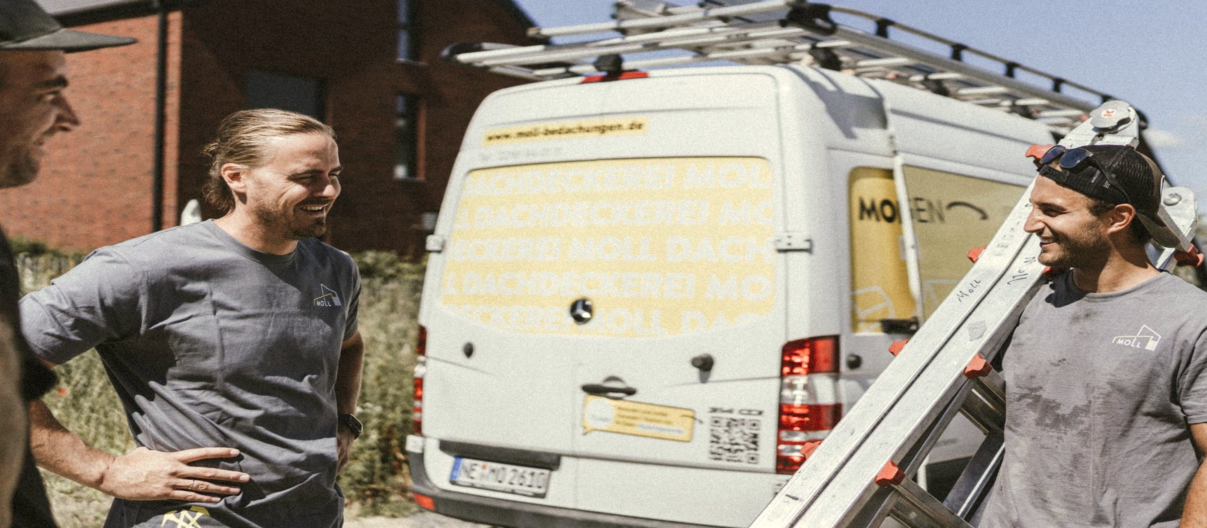 Drei Mitglieder vom Moll-M-Team vor dem Moll-Dachdeckerei-Sprinter — lachendes Gespräch nach Feierabend