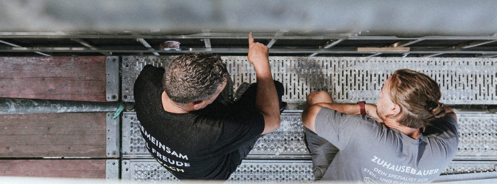 Zwei Dachdecker des M-Teams stimmen sich auf dem Gerüst ab — Aufnahme von oben