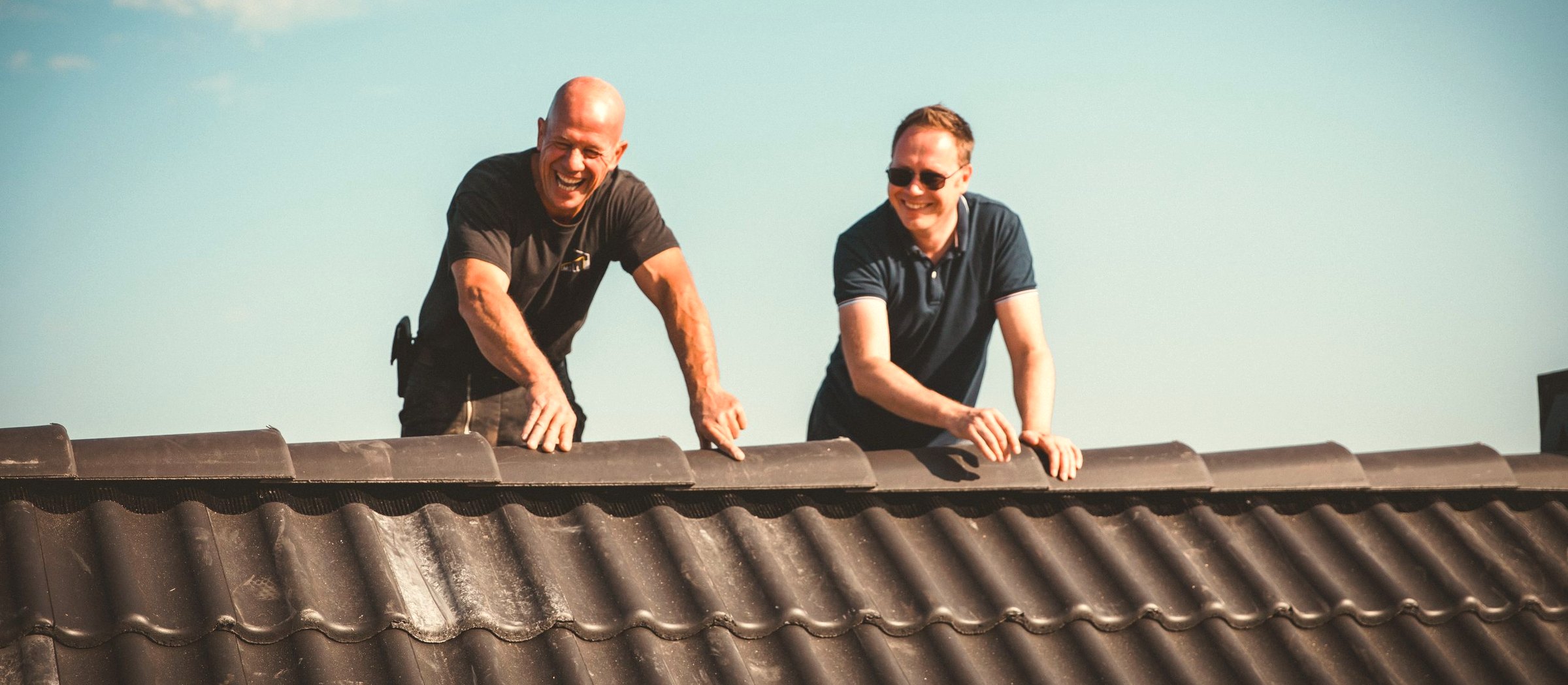 Zwei lächelnde Moll-Dachdecker bei der Arbeit auf einem fertig gedeckten Steildach